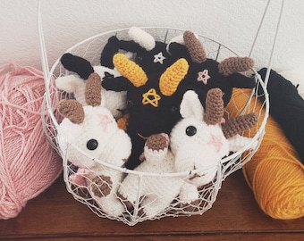 May include: A white wire basket filled with crocheted amigurumi toys. The toys are a variety of colors, including black, white, brown, and yellow. The basket has a wooden handle and is sitting on a wooden surface. The text "Crochet Pattern" is written in a white oval on top of the basket.