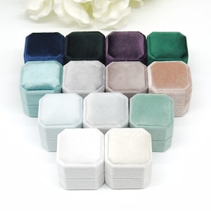 May include: A set of 10 velvet ring boxes in various colours, including navy blue, green, purple, light blue, grey, and beige. The boxes are arranged in a pyramid shape, with the largest box at the bottom and the smallest box at the top.