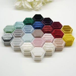 Op de afbeelding: Een verzameling zeshoekige fluwelen ringendoosjes in diverse kleuren, waaronder groen, blauw, roze en geel. De doosjes zijn gerangschikt in een honingraatpatroon, wat hun geometrische ontwerp en zachte textuur benadrukt.