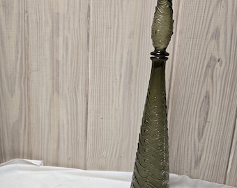 Puede incluir: Un decantador de vidrio verde oliva, alto y esbelto, con un tapón puntiagudo a juego. El cuerpo del decantador y el tapón presentan un patrón continuo en relieve de ondas giratorias que envuelve toda la superficie del vidrio.