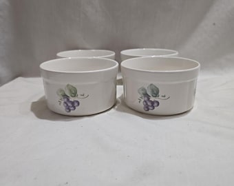 Puede incluir: Cuatro cuencos de cerámica blanca con forma redondeada. Cada cuenco presenta un diseño pintado de hojas verdes y uvas moradas. Los cuencos están dispuestos sobre una superficie blanca.