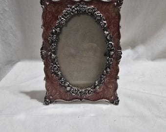 Puede incluir: Un marco de fotos vintage ornamentado, con un interior marrón rojizo y un borde floral plateado. El marco tiene una abertura ovalada y probablemente está hecho de metal. El diseño es detallado y elegante, adecuado para exhibir una fotografía preciada.