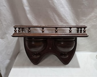 Puede incluir: Estante de pared de madera marrón oscuro con una barandilla decorativa y dos compartimentos en forma de cuenco. El estante está hecho de madera y tiene un diseño clásico, adecuado para exhibir objetos pequeños o decoración.