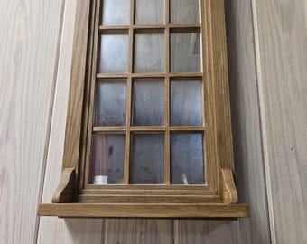 Puede incluir: Un marco de ventana rectangular de madera con un acabado marrón medio, que presenta una cuadrícula de doce paneles de vidrio individuales dispuestos en tres columnas y cuatro filas. Un pequeño estante de madera plano está unido a la parte inferior con dos soportes curvos.