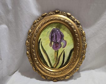Puede incluir: Pintura ovalada de una flor de iris púrpura en un marco dorado ornamentado. El iris está centrado en un fondo verde claro con hojas verdes oscuras y un tallo marrón. El marco tiene un diseño detallado y texturizado.