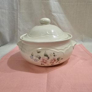 Può includere: Piatto da forno in ceramica bianca con un design floreale con fiori rosa, viola e verdi. Il piatto ha un coperchio con un pomo in cima.