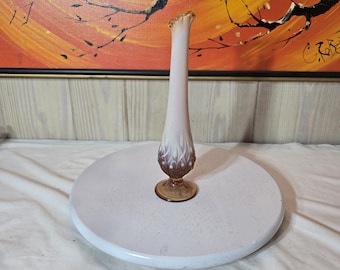 Puede incluir: Un florero alto y esbelto de vidrio con un borde ondulado. El florero presenta un diseño degradado, que transita de un blanco translúcido en la parte superior a un marrón ámbar profundo en la base, acentuado con patrones de gotas blancas.