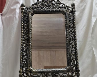 Puede incluir: Espejo rectangular ornamentado con acabado en bronce oscuro. El marco presenta intrincados adornos y soportes en forma de columna retorcida. El espejo es una pieza decorativa, adecuada para montaje en pared.