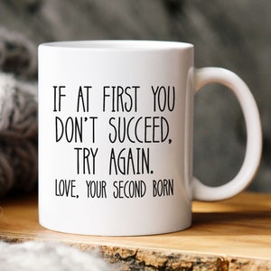 May include: White ceramic coffee mug with black text that reads "If at first you don't succeed, try again. Love, your second born."