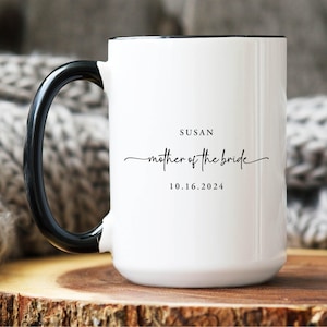May include: A white ceramic mug with a black handle and interior rim. The front features black printed text that reads SUSAN, followed by the script text mother of the bride, and the date 10.16.2024 centered below the text.