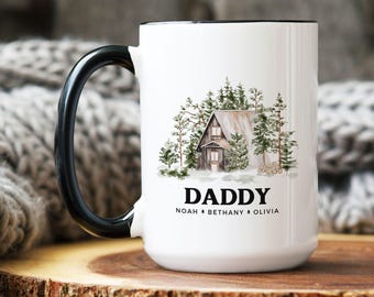 May include: A white ceramic mug with a black handle and rim, featuring a watercolor illustration of a cabin nestled in a pine forest. Below the cabin, the word DADDY is printed in black, followed by the names NOAH, BETHANY, and OLIVIA in smaller text.