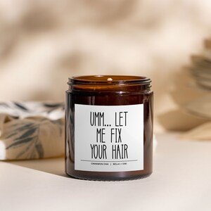 May include: A brown glass candle jar with a white label that reads "Umm... Let Me Fix Your Hair". The candle is labeled with the scent "Cinnamon Chai | Bella + Oak".