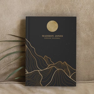 May include: Black dream journal with gold foil lettering that reads "MADISON JONES DREAM JOURNAL". The cover features a gold moon and a stylized mountain range with a starry night sky background.
