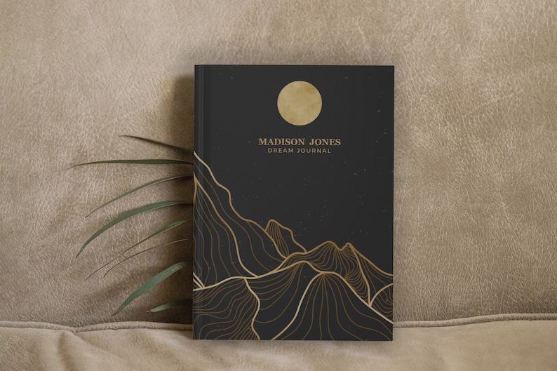 May include: Black dream journal with gold foil lettering that reads "MADISON JONES DREAM JOURNAL". The cover features a gold moon and a stylized mountain range with a starry night sky background.