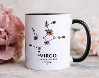 May include: A white ceramic mug with a black handle and rim, featuring a floral constellation design representing the Virgo zodiac sign. Below the graphic, the text reads VIRGO, loyal, practical, kind, and the name reagan in script font.