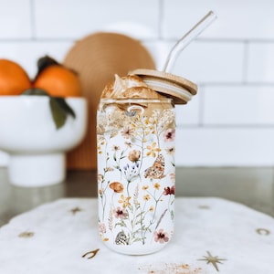 May include: A glass tumbler with a floral pattern and a wooden lid. The tumbler is filled with a creamy beverage and a clear straw.
