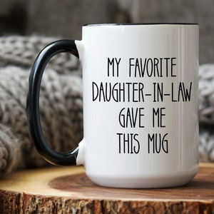 May include: White ceramic mug with a black rim and handle. The mug has black text that reads "My favourite daughter-in-law gave me this mug".