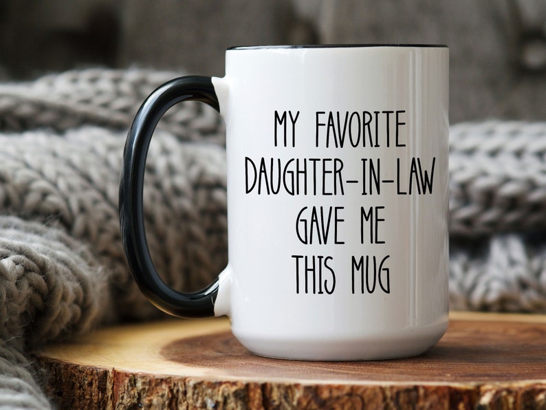 May include: White ceramic mug with a black rim and handle. The mug has black text that reads "My favourite daughter-in-law gave me this mug".