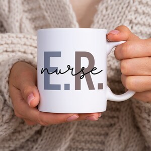 Pode incluir: Caneca de cer&acirc;mica branca com o texto "E.R. nurse" em letras pretas, cinzas e marrons.