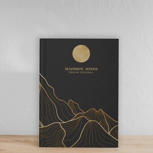May include: Black dream journal with gold foil accents. The cover features a stylized moon and mountains with the text "MADISON JONES DREAM JOURNAL".
