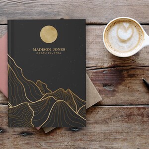 May include: A black dream journal with a gold moon and mountain design. The text "MADISON JONES DREAM JOURNAL" is printed on the cover.