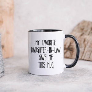 May include: White ceramic mug with a black rim and handle. The mug has black text that reads "My favourite daughter-in-law gave me this mug."