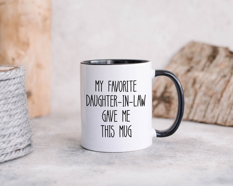 May include: White ceramic mug with a black rim and handle. The mug has black text that reads "My favourite daughter-in-law gave me this mug."