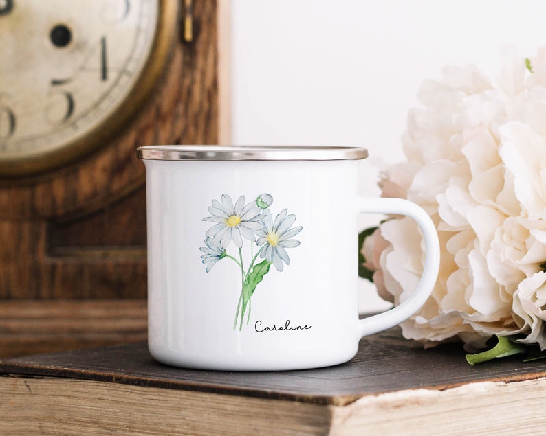 Puede incluir: Taza de esmalte blanco con borde plateado y una ilustraci&oacute;n de acuarela de margaritas blancas con tallos verdes. La taza tiene el nombre "Caroline" escrito en cursiva negra en la parte inferior.