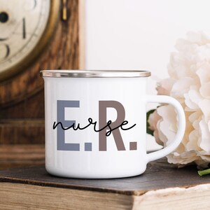 Pode incluir: Caneca de esmalte branco com borda prateada. A caneca tem o texto "E.R. nurse" impresso em preto, cinza e marrom.