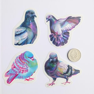 Puede incluir: Cuatro pegatinas troqueladas con palomas pintadas en varias poses y colores vibrantes, incluyendo tonos azules, morados y rosas. Una moneda de color plateado está colocada junto a la pegatina inferior derecha para mostrar la escala, con 2 cm de diámetro.