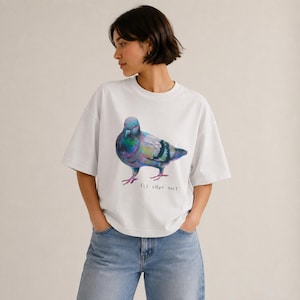 Puede incluir: Una camiseta blanca de manga corta con una colorida ilustración de una paloma con plumas iridiscentes en tonos morados, verdes y azules. Debajo del ave, el texto "FLY VIBES ONLY" está impreso en una fuente negra sencilla y manuscrita.