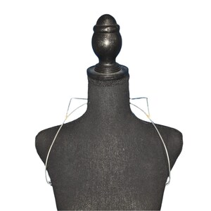 Puede incluir: Un maniquí negro con un sujetador de alambre plateado en la parte superior. El maniquí tiene una cabeza redonda con una tapa negra en la parte superior.