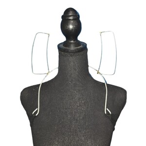 Puede incluir: Un maniquí negro con un par de gafas de alambre plateado drapeadas sobre los hombros.