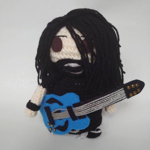 May include: Crocheted plush toy of a person with long black hair, wearing a black shirt and holding a blue electric guitar with silver strings.