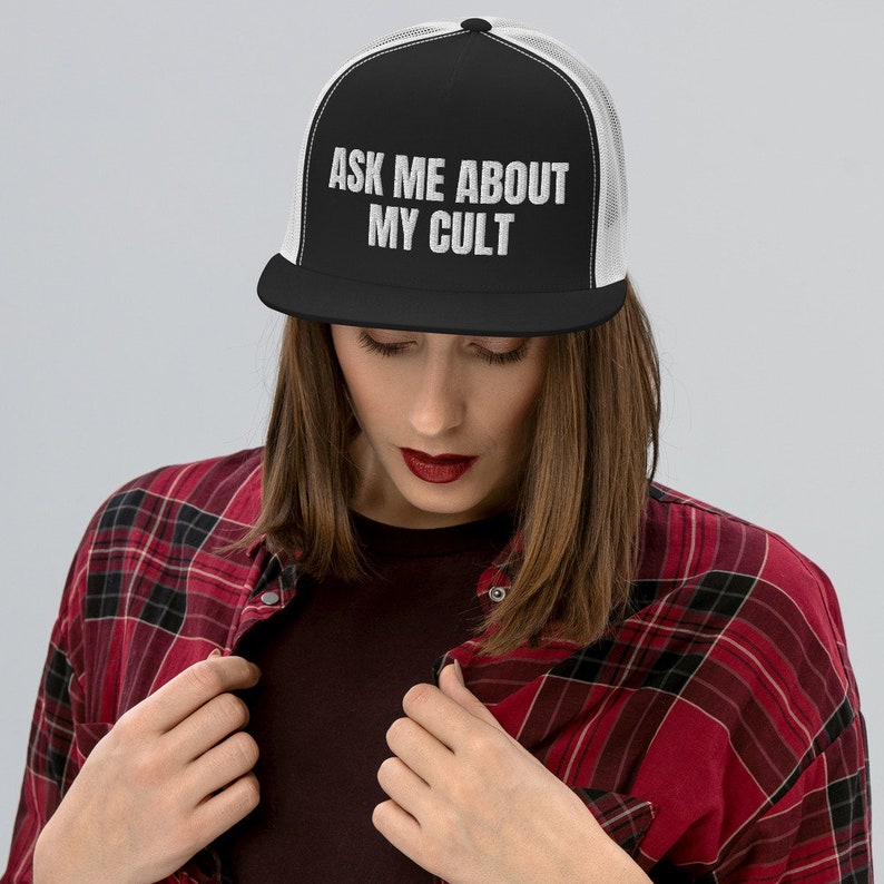 Puede incluir: Una gorra de camionero negra y blanca con una malla blanca en la parte posterior. La gorra tiene el texto "ASK ME ABOUT MY CULT" en letras blancas en la parte delantera.