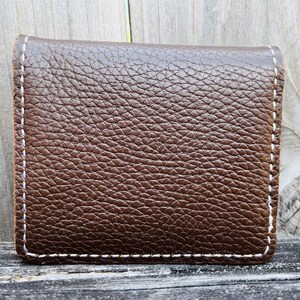 May include: A brown leather wallet with white stitching around the edges.