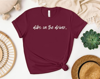Könnte beinhalten: Burgunderfarbenes T-Shirt mit weißem Text, der "dibs on the driver." lautet.