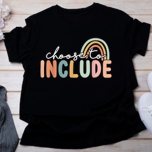 May include: Black t-shirt with the words "choose to INCLUDE" in a colorful, rainbow-themed design. The text is in a playful font, with the word "INCLUDE" in large, block letters. A rainbow graphic sits above the word "INCLUDE".