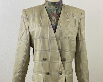 May include: A tan plaid skirt suit with a double-breasted blazer. The blazer has four buttons and two front pockets. A patterned blouse is visible beneath the lapels. The skirt is a solid tan color.