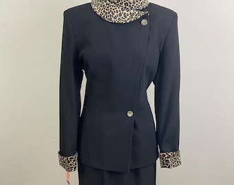 May include: A black suit with a skirt and jacket. The jacket has a high collar with a leopard print trim. The cuffs of the jacket also have a leopard print trim.