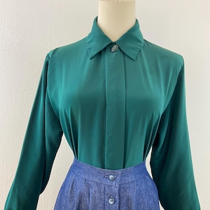 May include: A teal green long-sleeve blouse with a buttoned collar and a blue denim skirt. The skirt has a button-down front. The outfit is displayed on a mannequin.