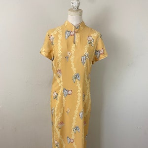 May include: A yellow maxi dress with a floral print and a mandarin collar. The dress has short sleeves and a fitted waist.