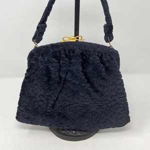 May include: A black velvet evening bag with a gold clasp and a bow. The bag has a short handle and is in good condition.