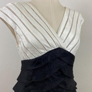 May include: A formal dress with a white, striped bodice and a black, layered skirt. The dress has a V-neck and is displayed on a mannequin. The dress is made of a shiny fabric.