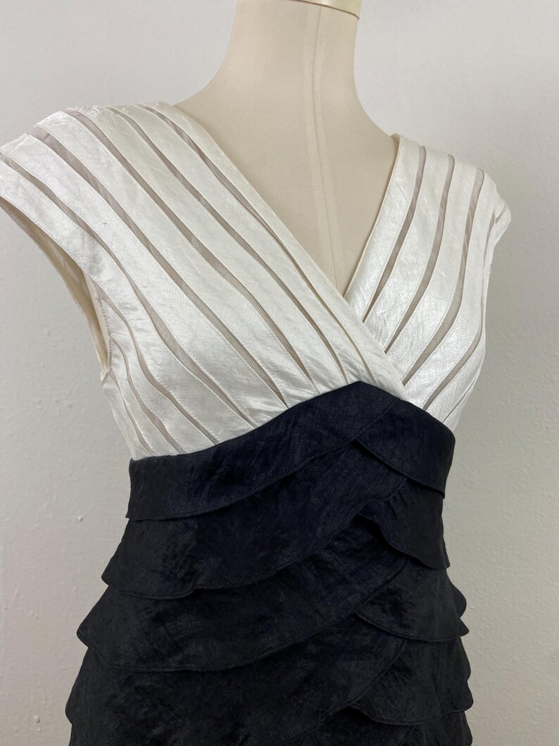 May include: A formal dress with a white, striped bodice and a black, layered skirt. The dress has a V-neck and is displayed on a mannequin. The dress is made of a shiny fabric.