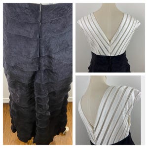 May include: A black and white formal dress with a tiered skirt and a V-neckline. The bodice is white with vertical stripes, and the skirt is black. The dress is displayed on a mannequin.