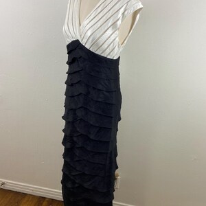 May include: A formal, floor-length dress with a V-neck bodice. The top is white with vertical striped detailing, transitioning to a black, tiered skirt. The dress is displayed on a mannequin.