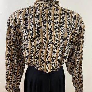 Peut inclure: Un chemisier vintage &agrave; manches longues avec un motif animalier unique dans les tons de marron, noir et cr&egrave;me. Le chemisier pr&eacute;sente un col montant et est associ&eacute; &agrave; un pantalon noir taille haute. Le tissu semble l&eacute;ger et adapt&eacute; &agrave; diverses occasions.