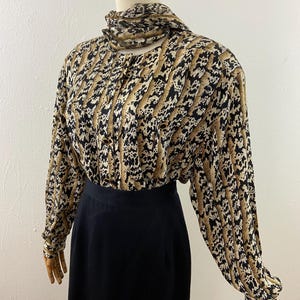 Peut inclure: Ensemble vintage compos&eacute; d'un chemisier et d'une jupe. Le chemisier &agrave; manches longues pr&eacute;sente un imprim&eacute; animalier beige, noir et blanc avec un col montant. La jupe noire est de longueur midi. L'ensemble est pr&eacute;sent&eacute; sur un mannequin.