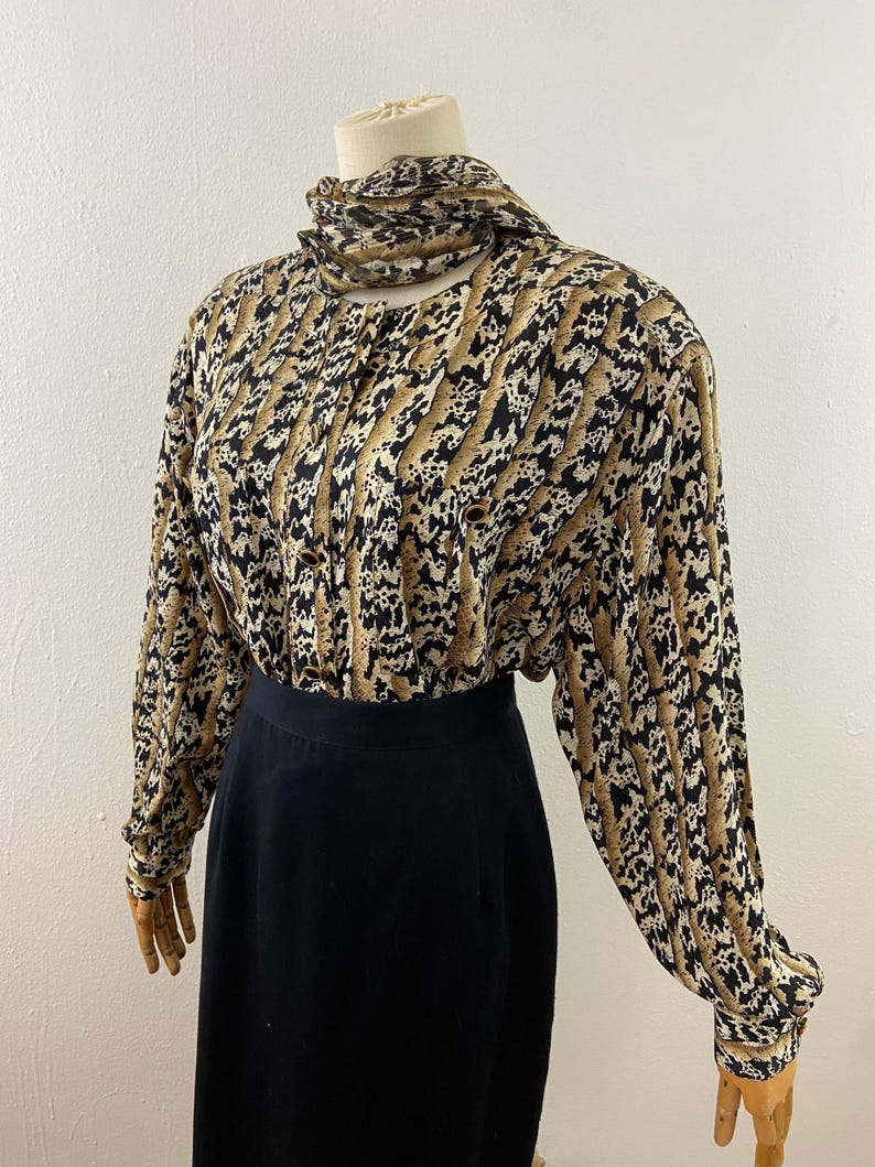 Peut inclure: Ensemble vintage compos&eacute; d'un chemisier et d'une jupe. Le chemisier &agrave; manches longues pr&eacute;sente un imprim&eacute; animalier beige, noir et blanc avec un col montant. La jupe noire est de longueur midi. L'ensemble est pr&eacute;sent&eacute; sur un mannequin.
